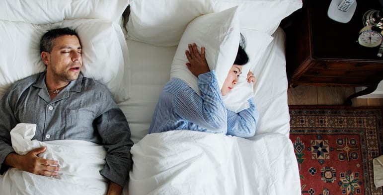 A woman trying to sleep while her husband is snoring in bed
