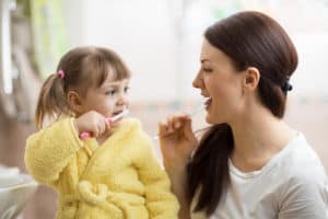 A mother teaching her daughter to brush her teeth