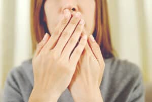 A woman with breath covering her mouth to hide her bad breath