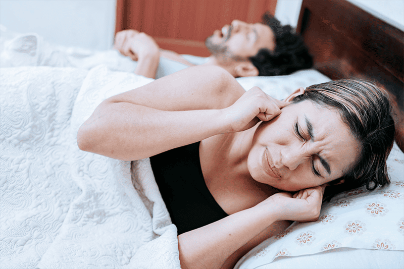 A man snoring and his wife plugging her ears