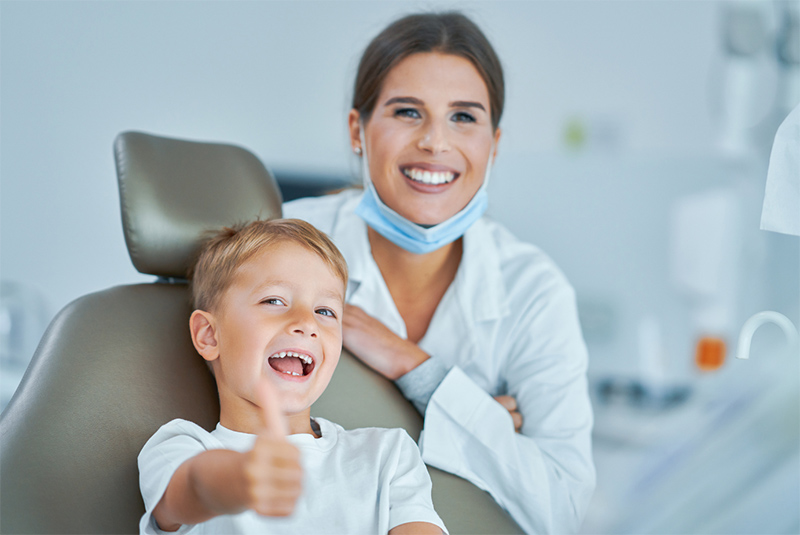 A smiling child sitting in a dental chair and giving a thumbs up